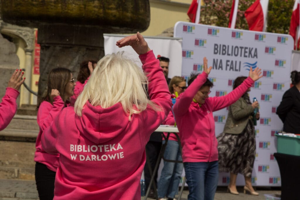 Osoby w różowych bluzach tańczą na wydarzeniu publicznym
