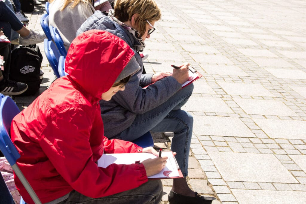 Osoby siedzące na krzesłach piszą na zewnątrz