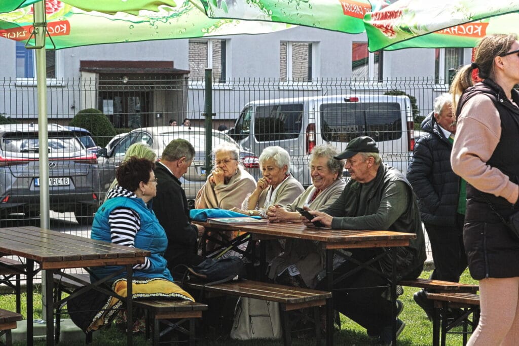 Starsze osoby siedzące przy drewnianym stole na zewnątrz