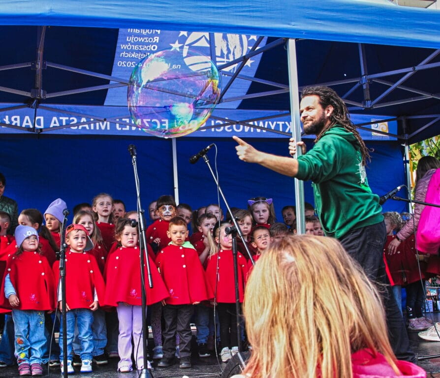Mężczyzna tworzy wielką bańkę mydlaną przed dziećmi w czerwonych płaszczykach
