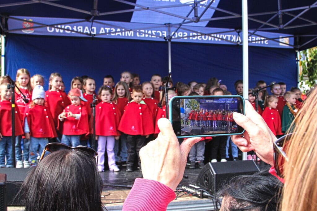 Dzieci w czerwonych płaszczykach śpiewają na scenie