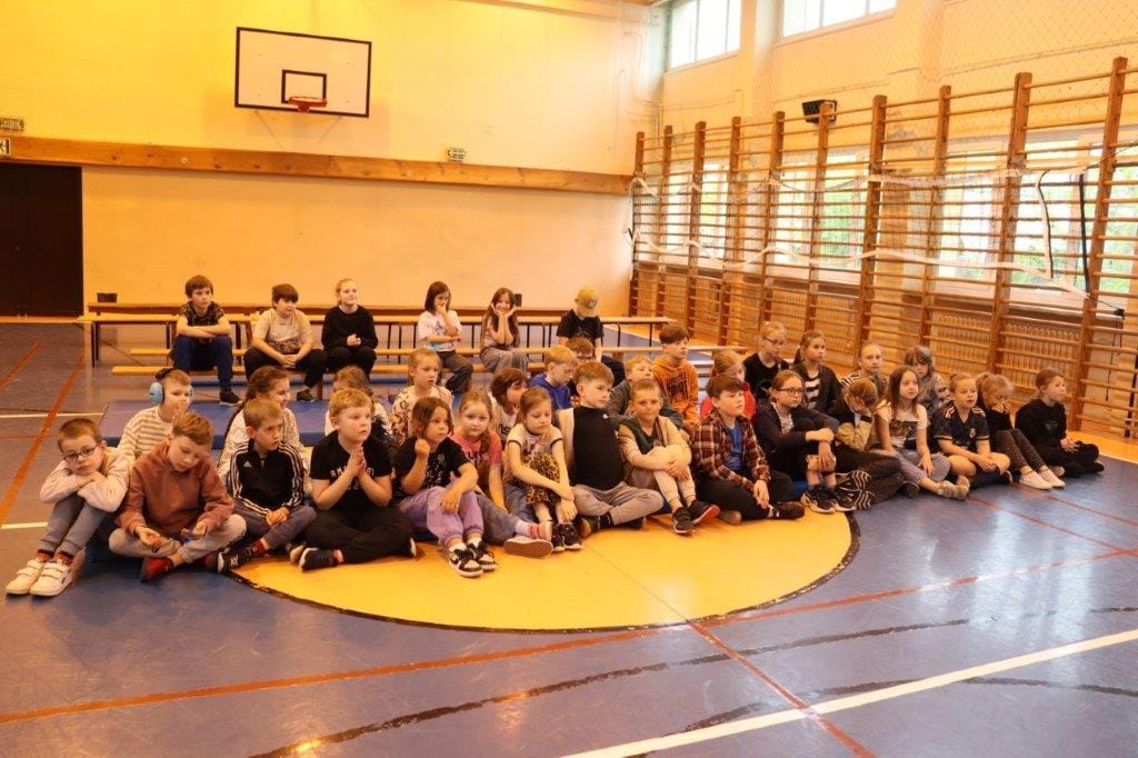Grupa dzieci siedzi na matach w sali gimnastycznej