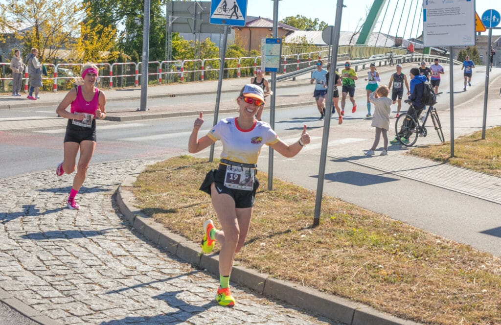 Kobieta biegnie w maratonie, robiąc znak 'ok'