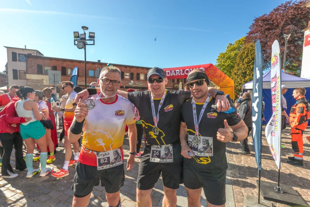 Trzech mężczyzn z medalami po maratonie, pokazujący kciuki