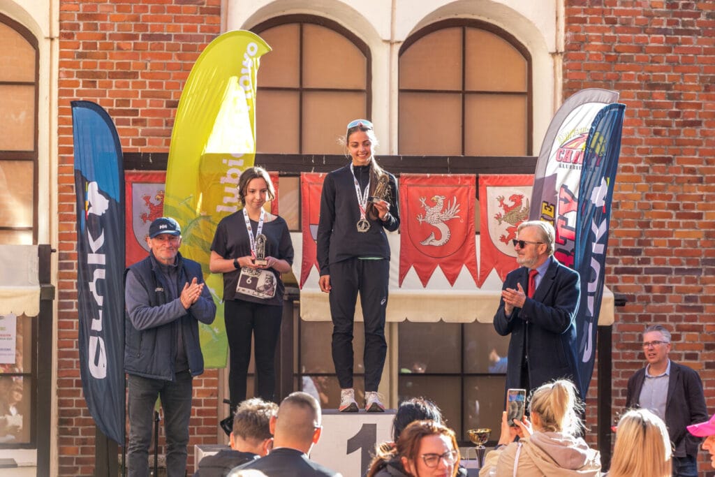 Uczestnicy odbierają medale na podium przy historycznym budynku