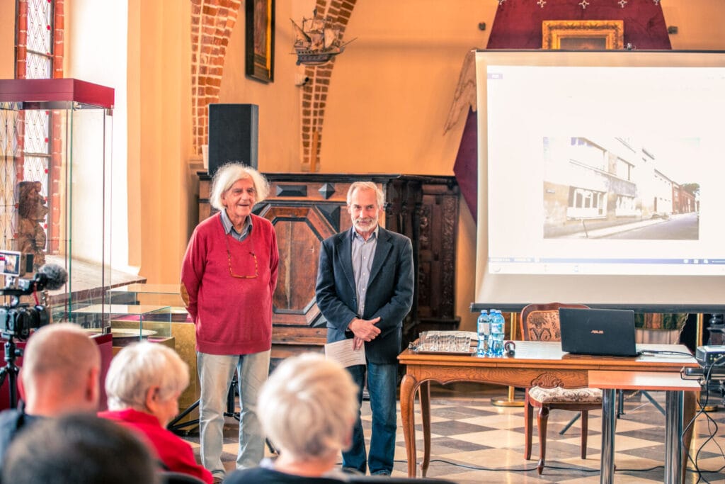 Dwaj mężczyźni prowadzą prezentację w zabytkowej sali