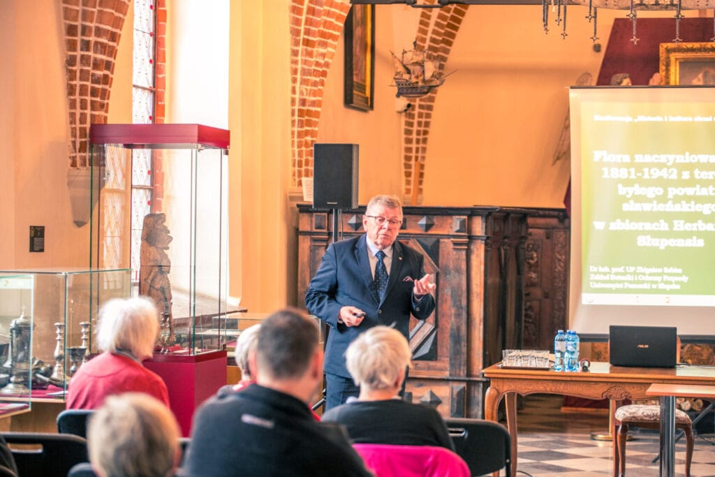 Starszy mężczyzna wygłasza prezentację w historycznej sali