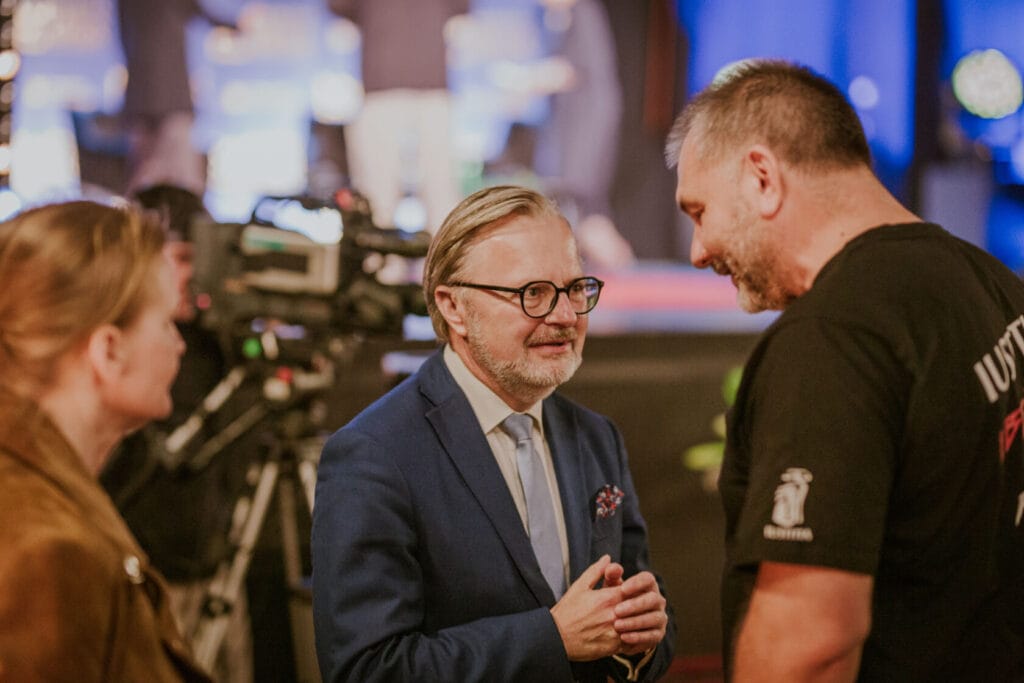 Mężczyźni rozmawiają w tłumie przy kamerze filmowej