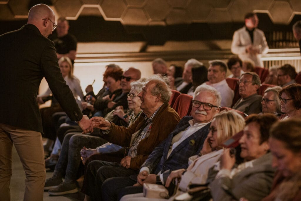 Starszy mężczyzna witający się z publicznością w teatrze
