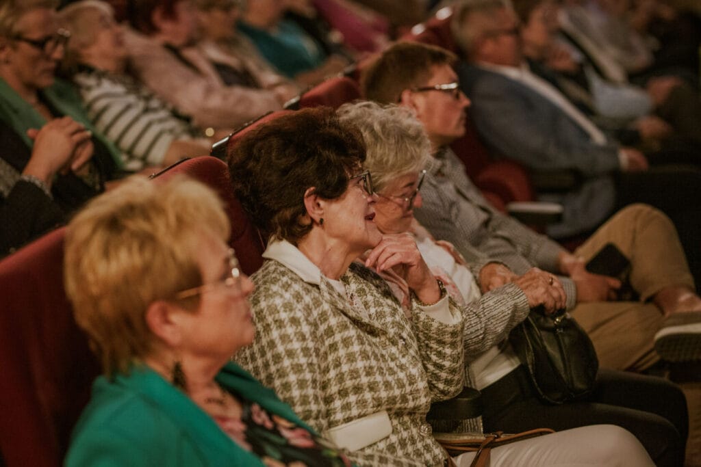 Starsi ludzie oglądający występ w teatrze.