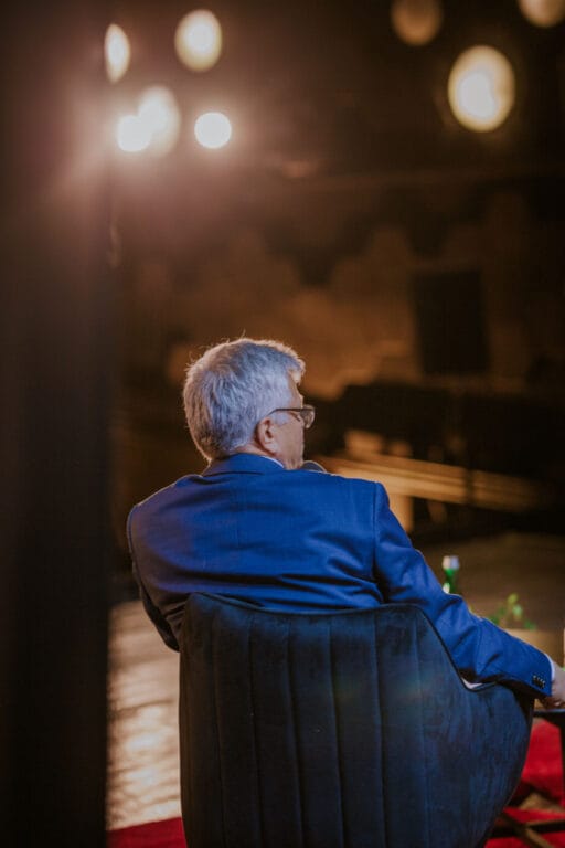 Mężczyzna w niebieskim garniturze siedzi przodem do reflektorów