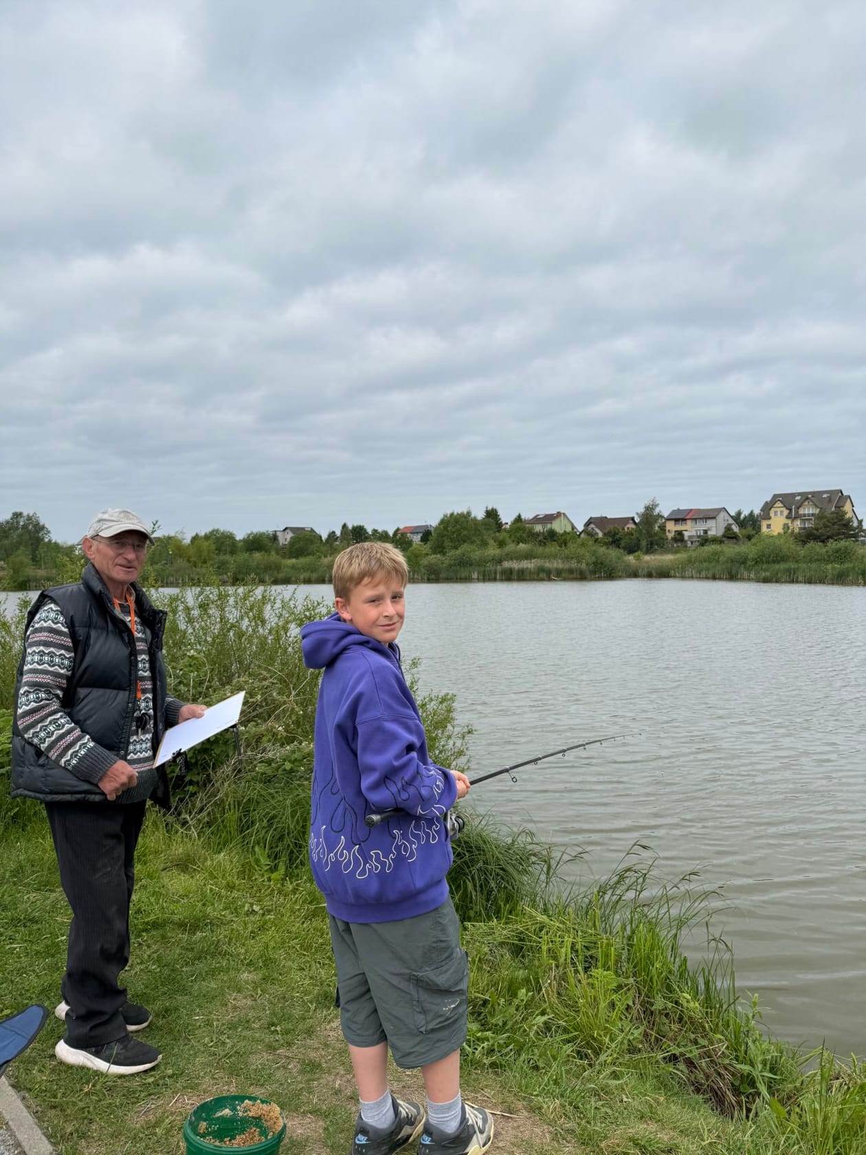 Starszy mężczyzna i chłopiec łowią ryby nad jeziorem.