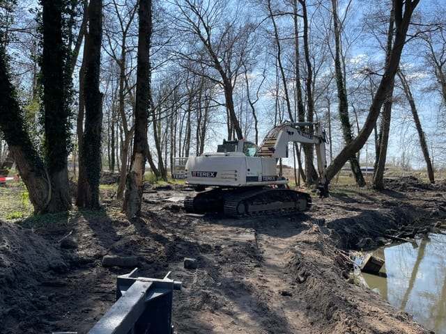 Koparka Terex pracuje w leśnej okolicy przy wodzie.