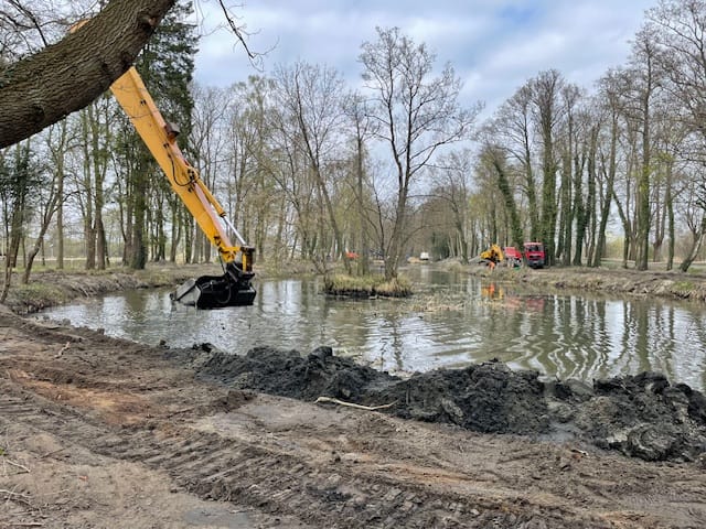 Koparka pracuje przy oczyszczaniu stawu w parku