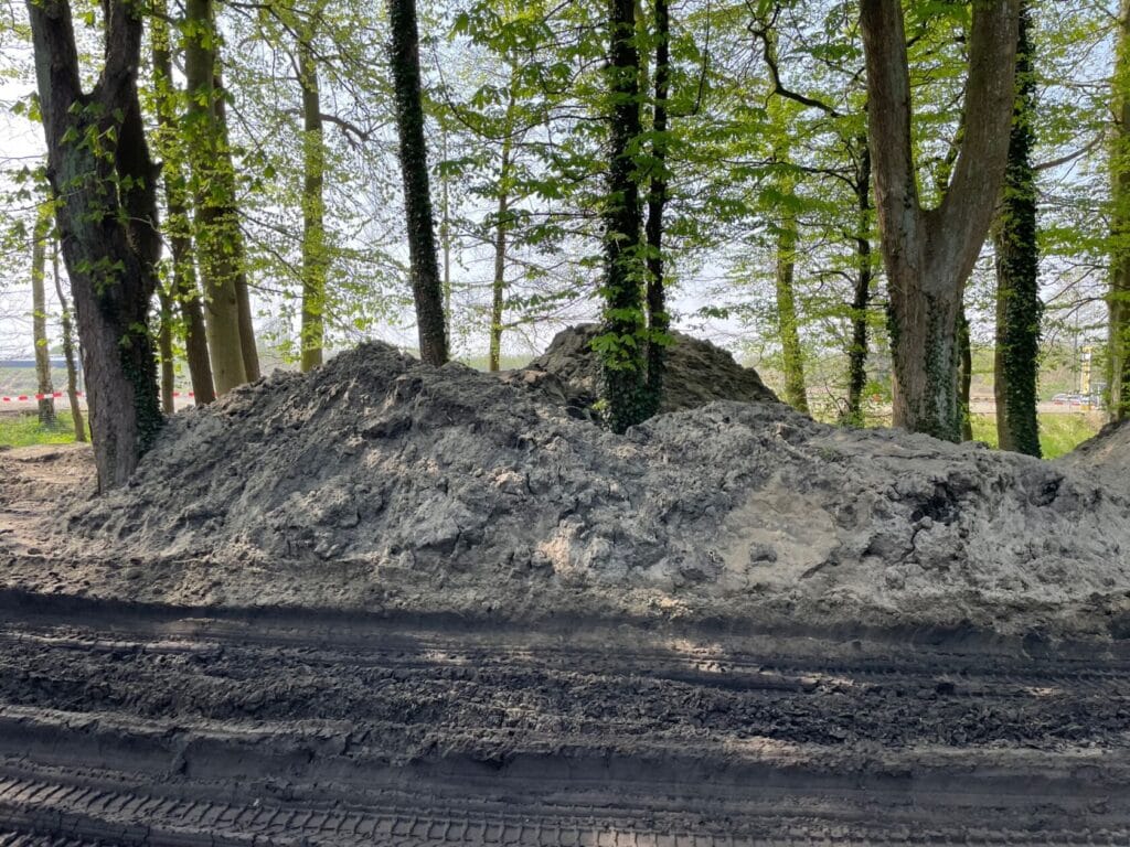 Kopiec ziemi na budowie przy drzewach.