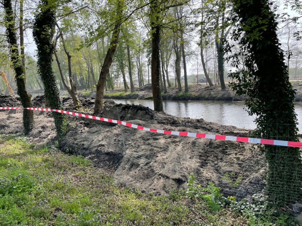 Teren budowlany przy rzece, ogrodzony czerwono-białą taśmą.