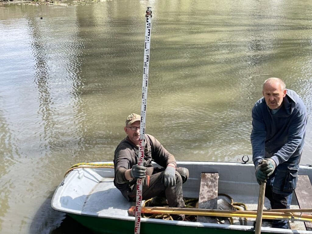 Dwóch mężczyzn w łodzi mierzy głębokość rzeki