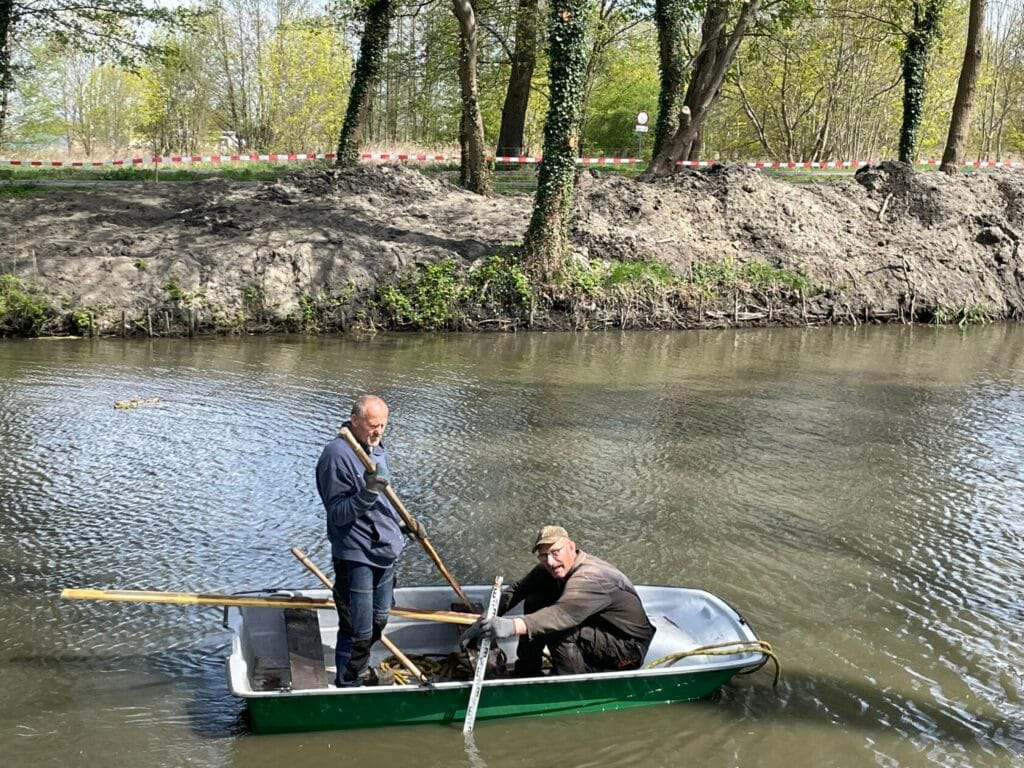 Dwaj mężczyźni w łódce na rzece, jeden wiosłuje.