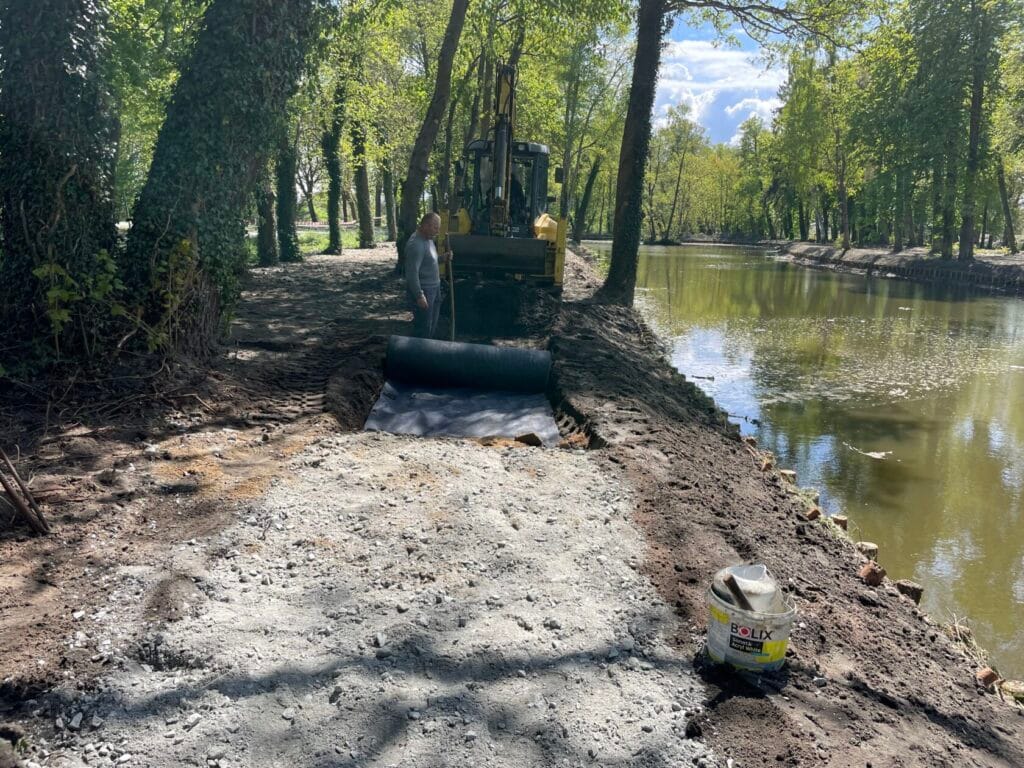 Prace modernizacyjne nad rzeką z koparką i materiałami budowlanymi