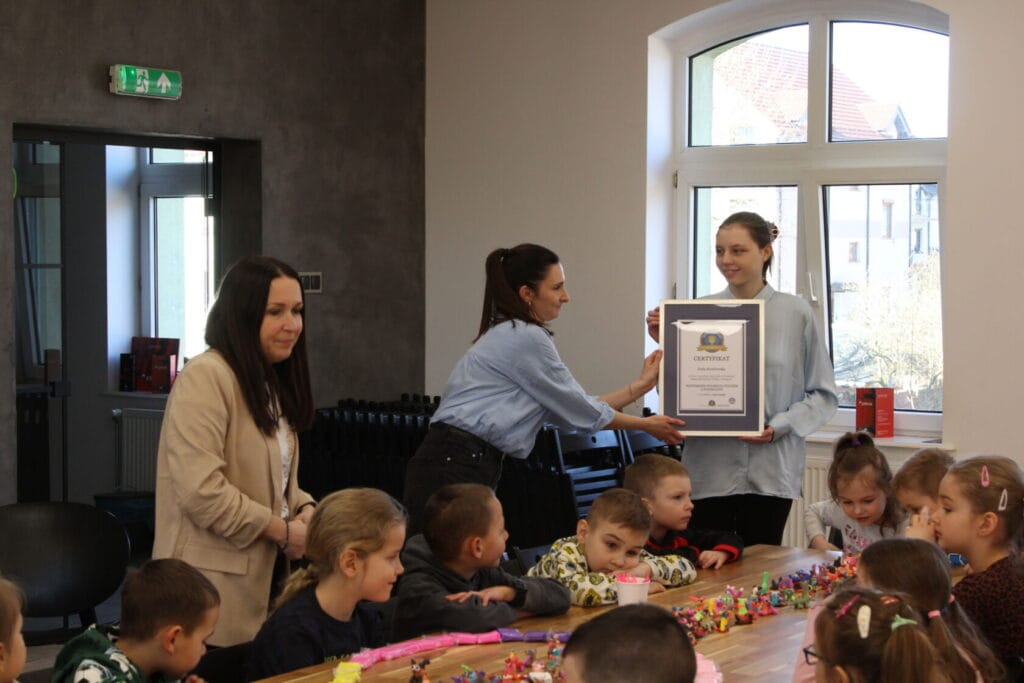 Kobieta wręcza certyfikat młodej dziewczynie w klasie