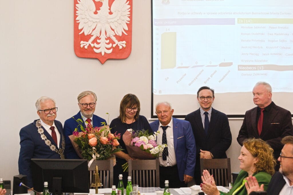 Grupa osób na spotkaniu z bukietami kwiatów.