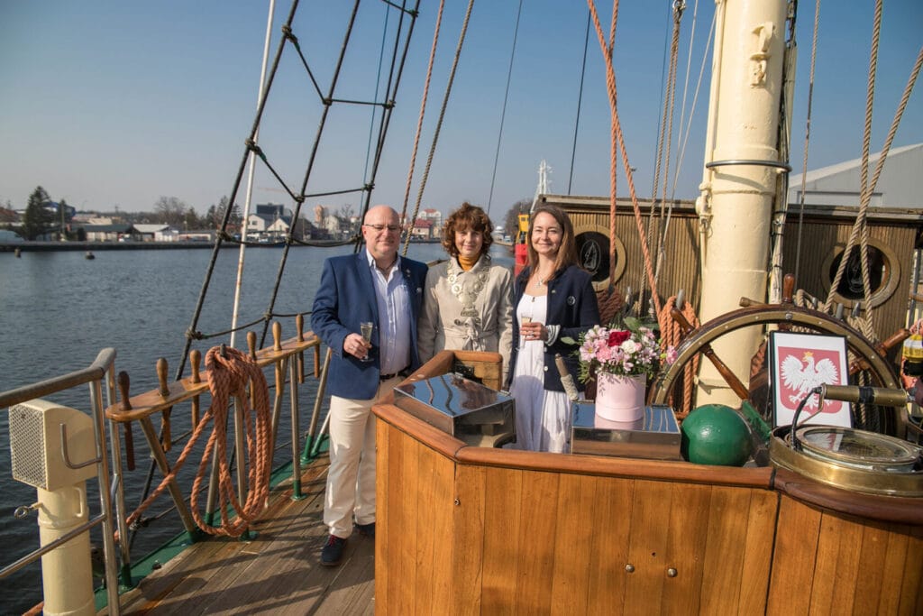 Trzy osoby na łodzi z drewnianą sterówką, rzeka, miasto