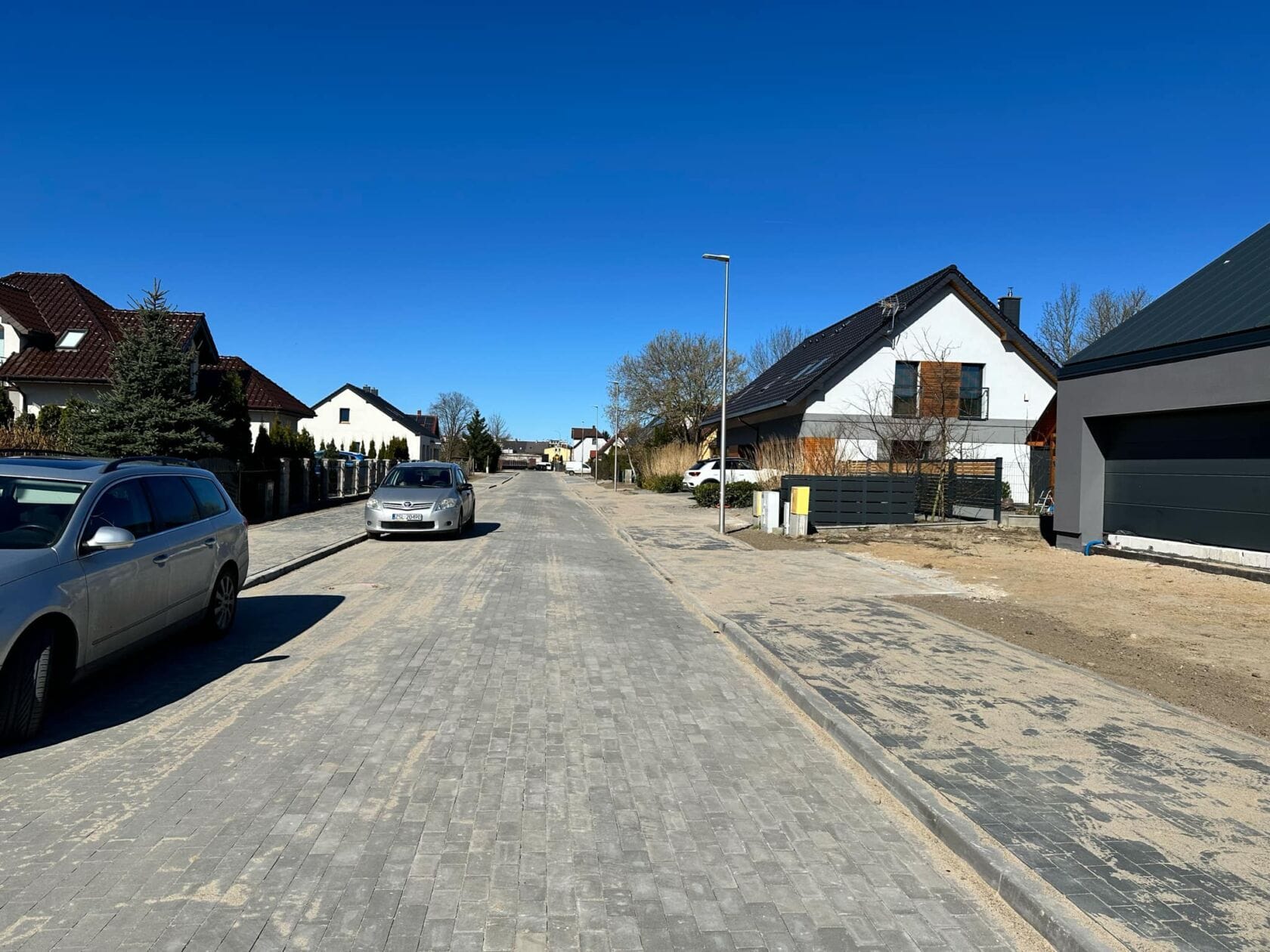 x32cGZFs Słoneczna ulica z domami i samochodami, niebieskie niebo