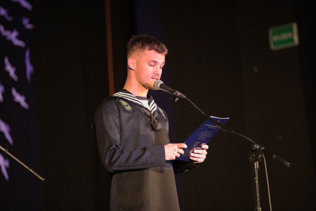 Młody mężczyzna w mundurze marynarki czyta ze sceny