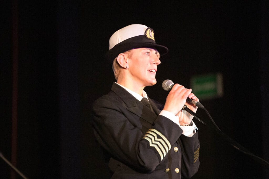 Kobieta w marynarce śpiewa do mikrofonu na scenie.