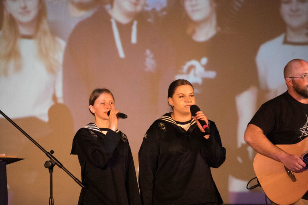 Dwie młode kobiety śpiewają na scenie z mikrofonami