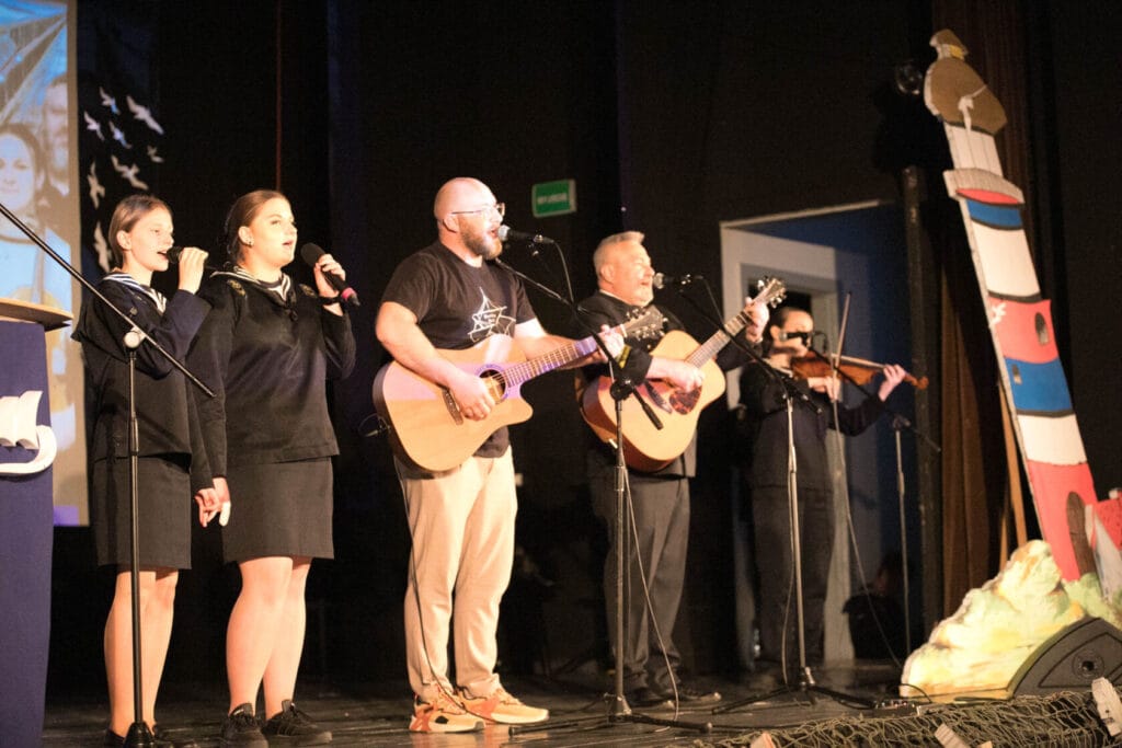 Grupa ludzi śpiewa i gra na gitarach na scenie