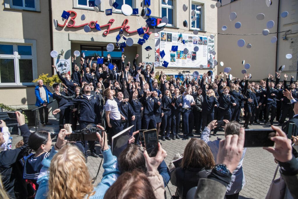 Uczniowie rzucają czapki w powietrze przed szkołą