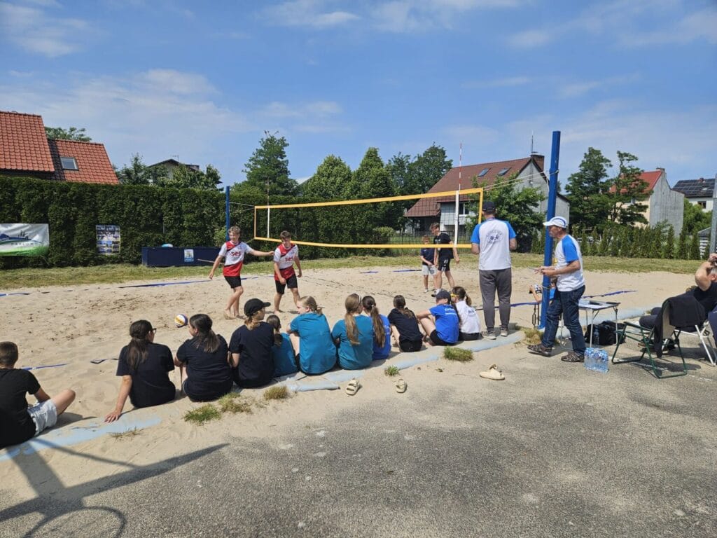 Dzieci oglądają mecz siatkówki plażowej w słoneczny dzień.