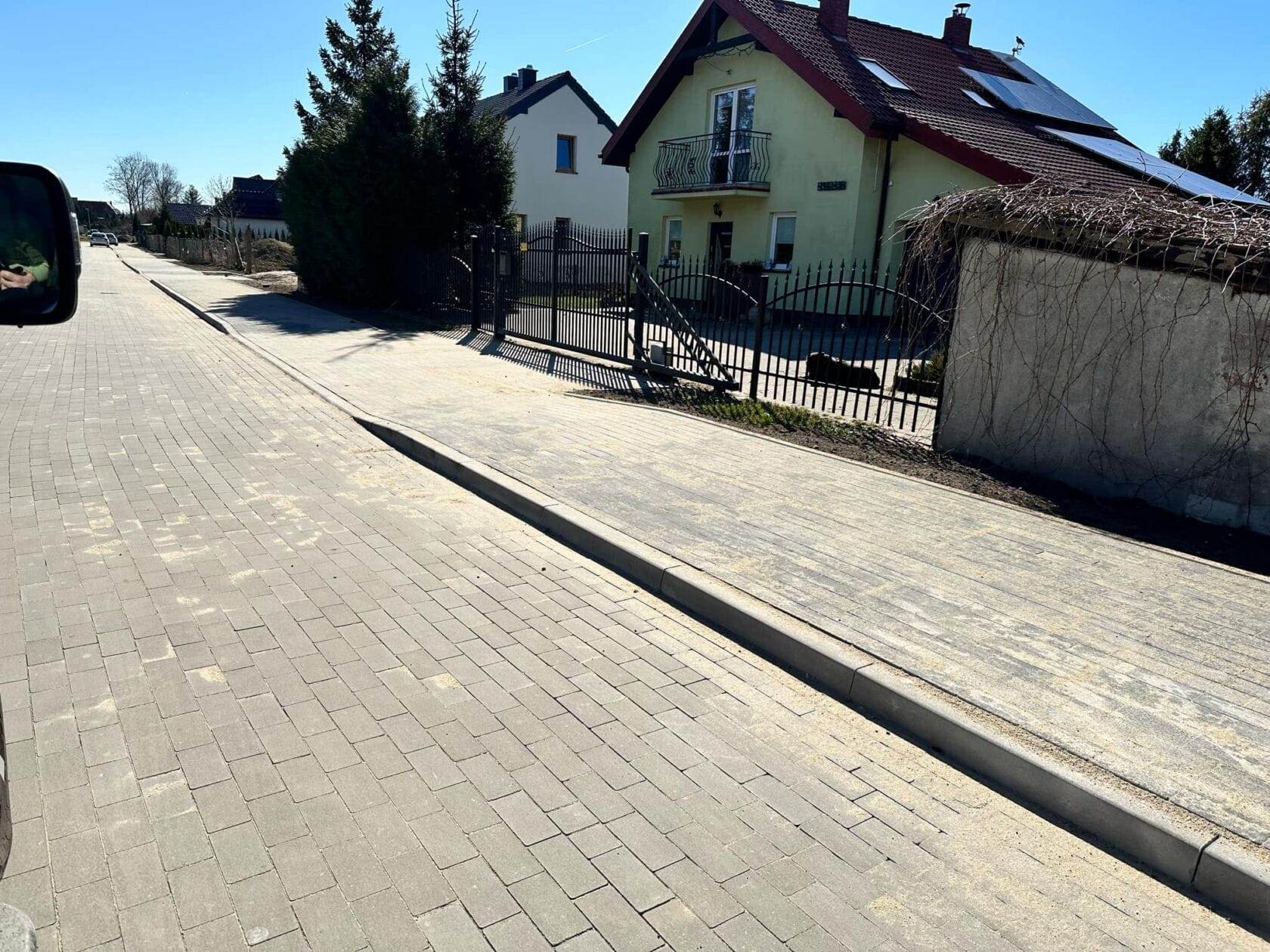 zqf1WxAk Słoneczna ulica z kostki brukowej i żółtym domem.