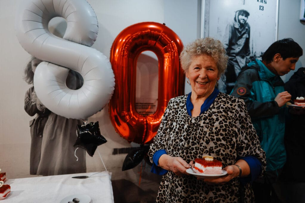 Starsza kobieta trzymająca tort przy balonach 80 urodziny